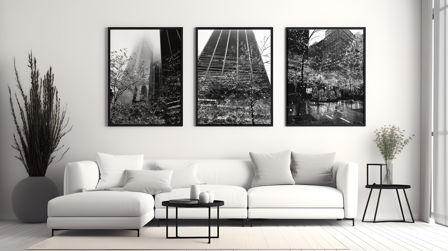 Three framed New York fairy light prints in black frames displayed on a white wall above a white corner sofa with cushions, with a black side table and plants on either side.