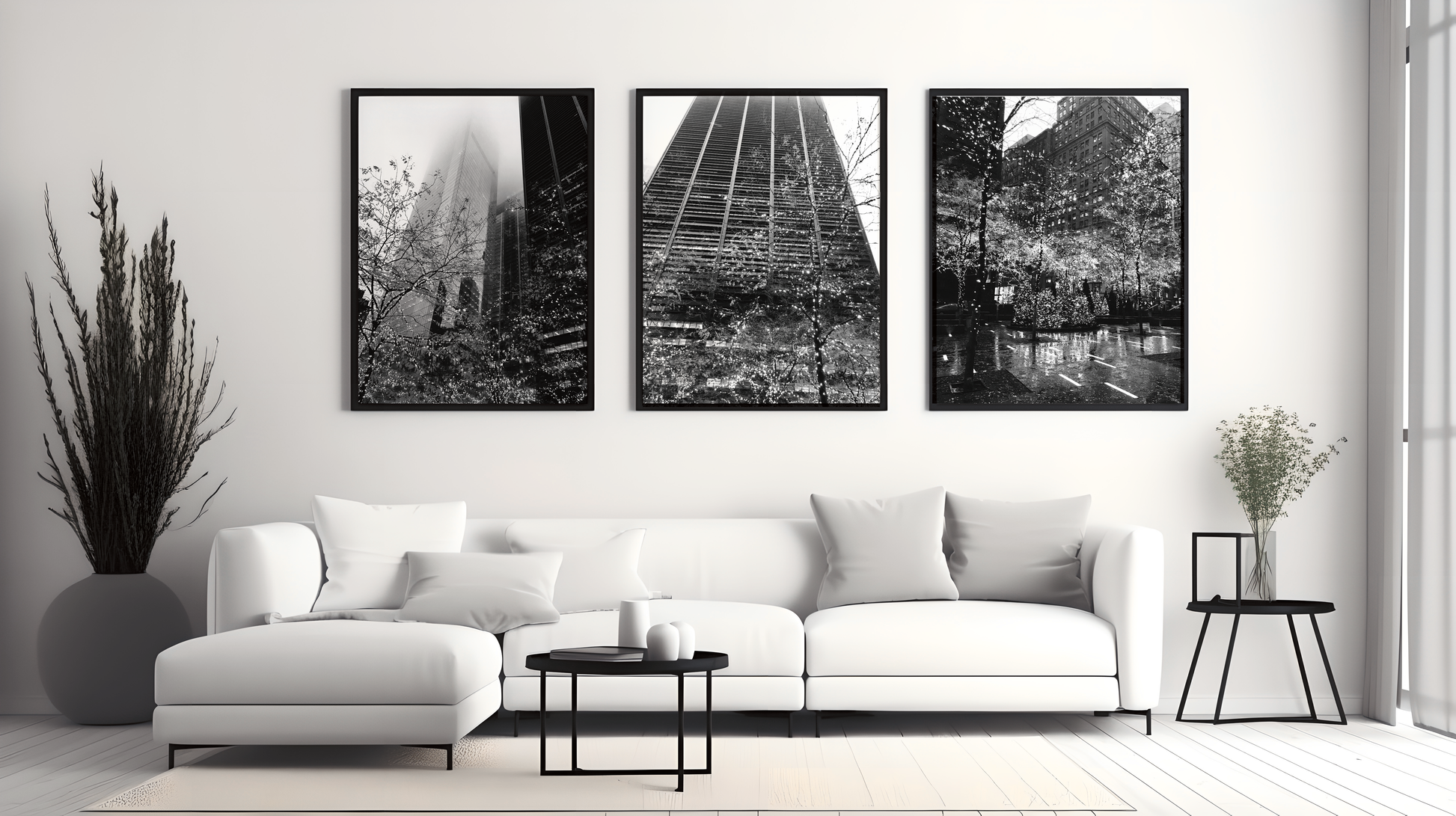 Three framed New York fairy light prints in black frames displayed on a white wall above a white corner sofa with cushions, with a black side table and plants on either side.
